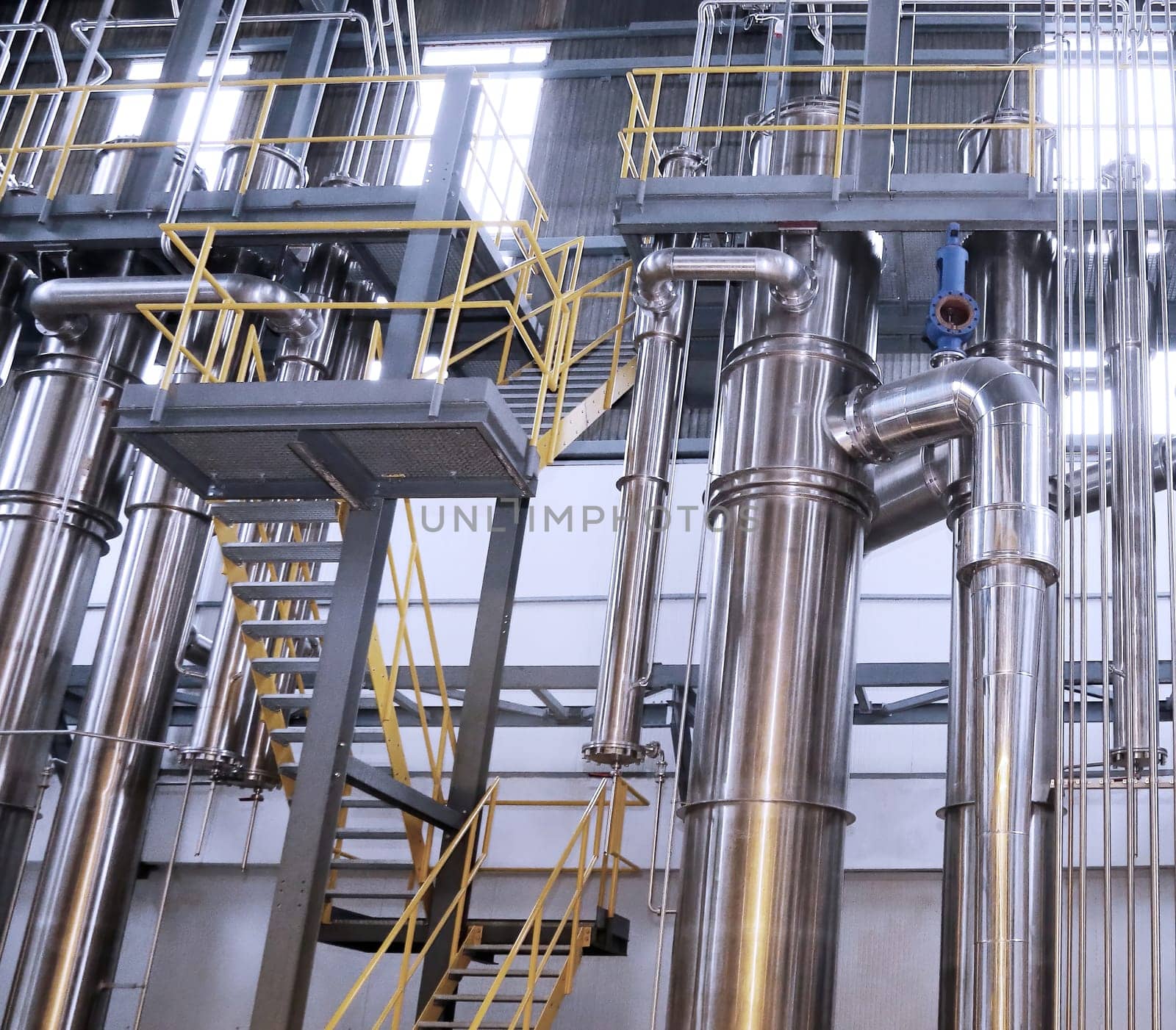 A chemical plant features a complex network of stainless steel pipes and glass vessels, creating an intricate system of interconnected straight and curved components in various sizes and shapes.