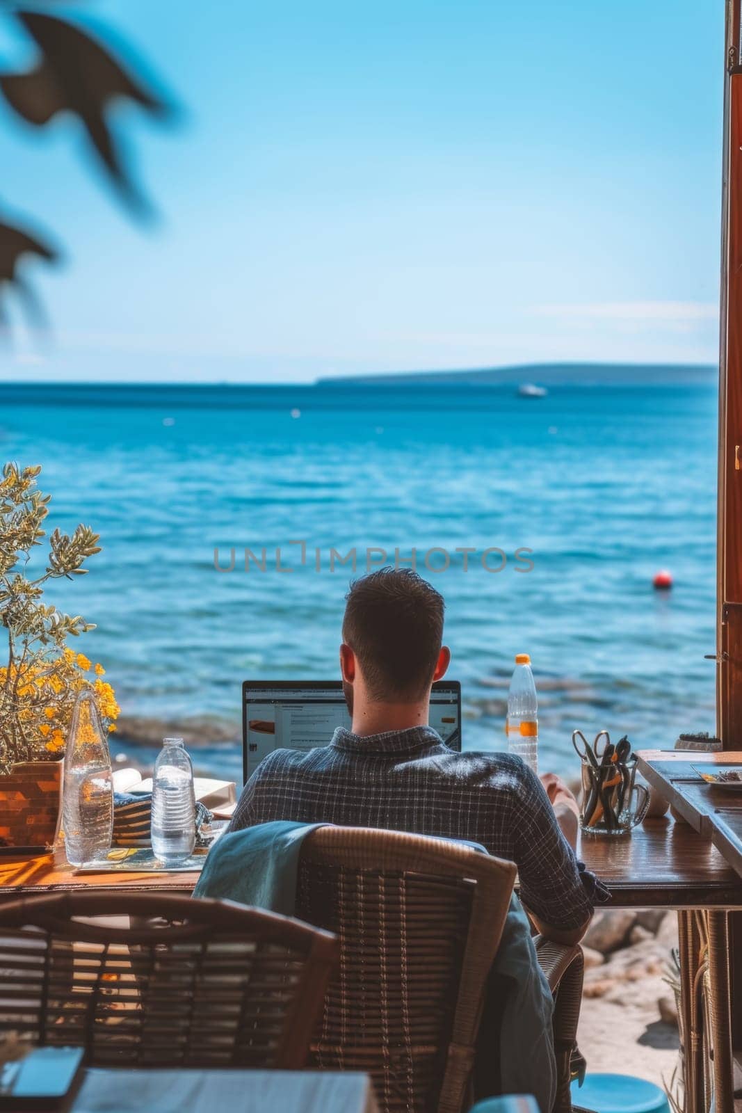 A person working on a laptop by the sea, surrounded by nature, under a clear sky