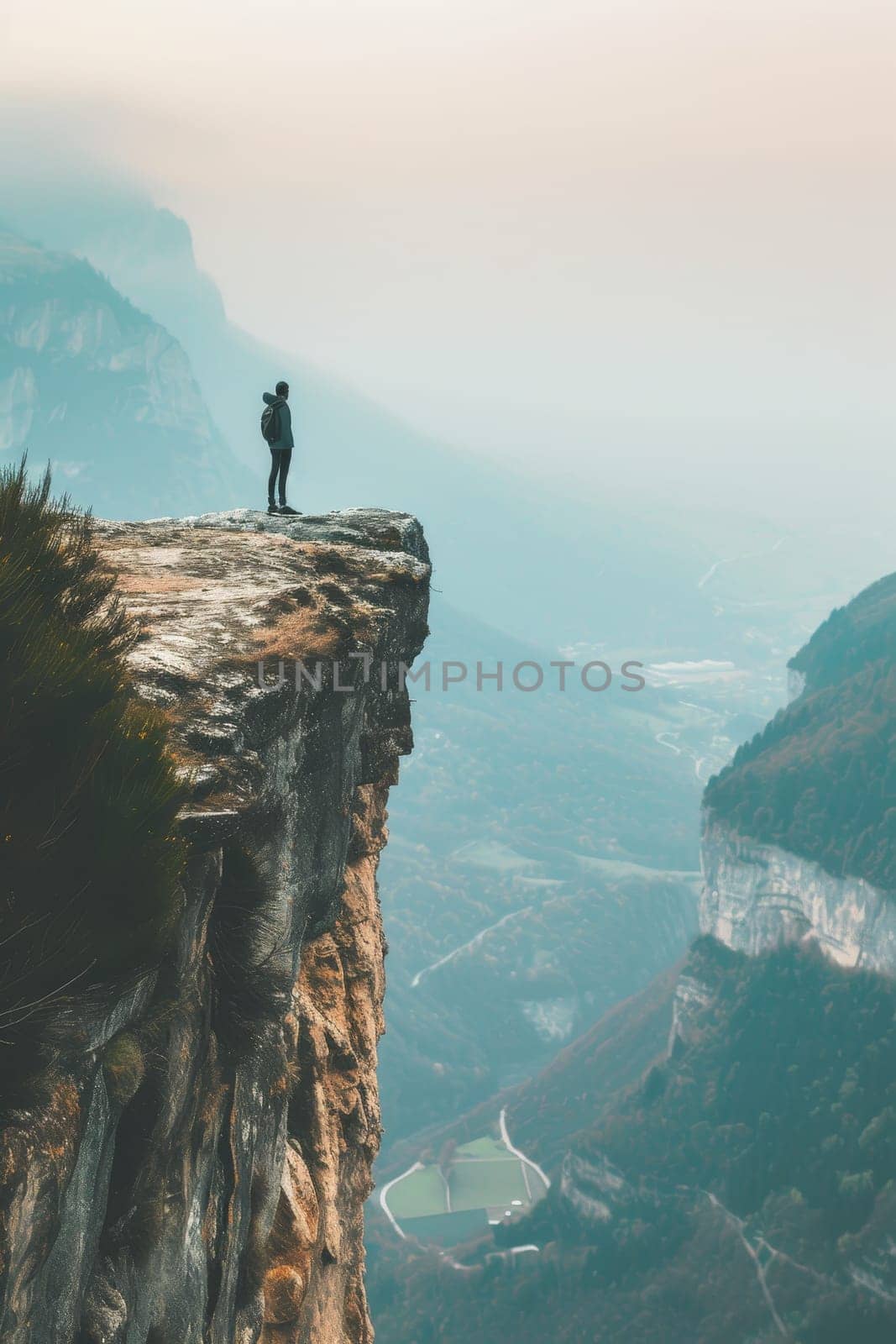 Person standing on a high cliff edge with a breathtaking view of a river and mountains during sunset