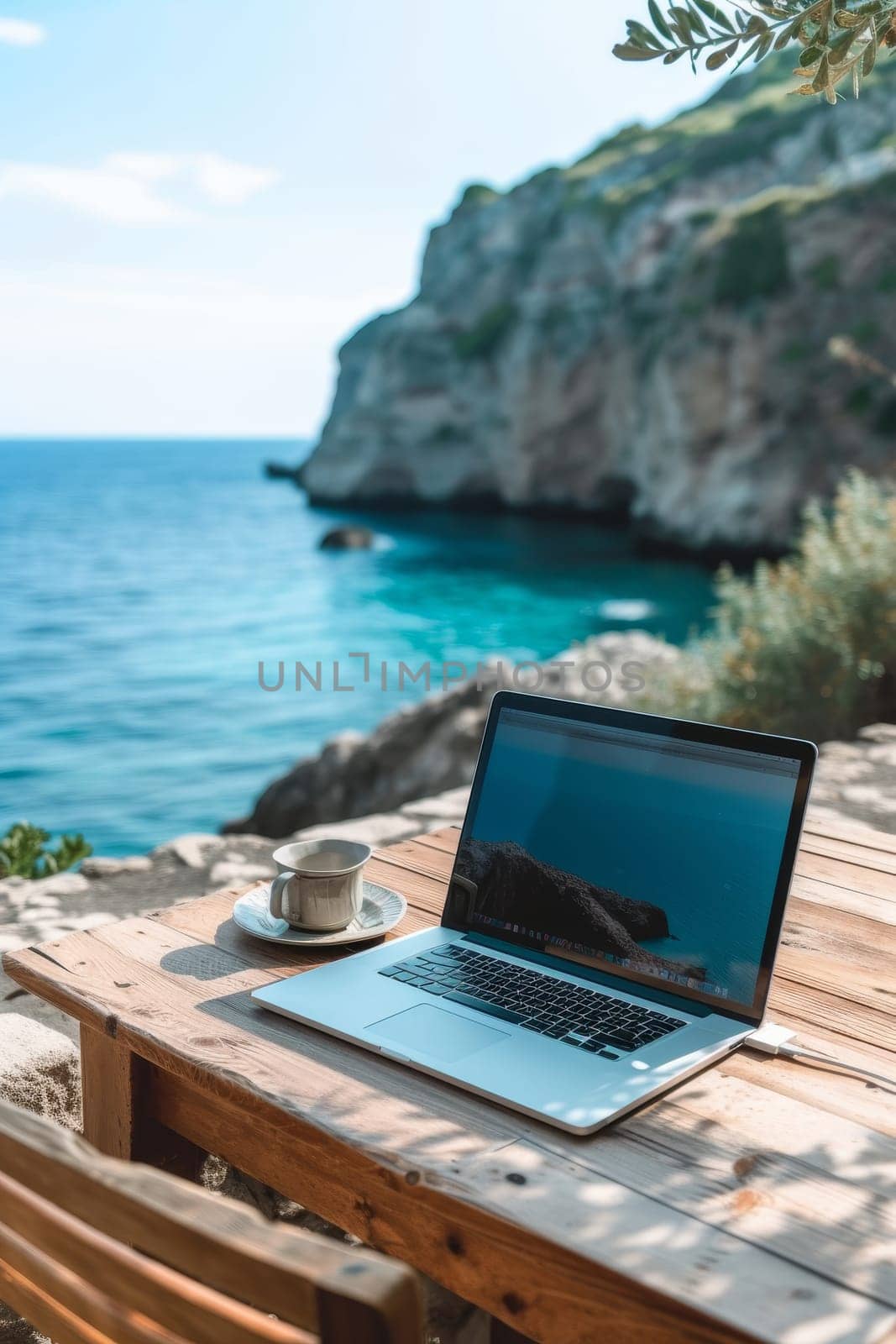 Laptop set up on a wooden table with a breathtaking view of the sea and cliffside