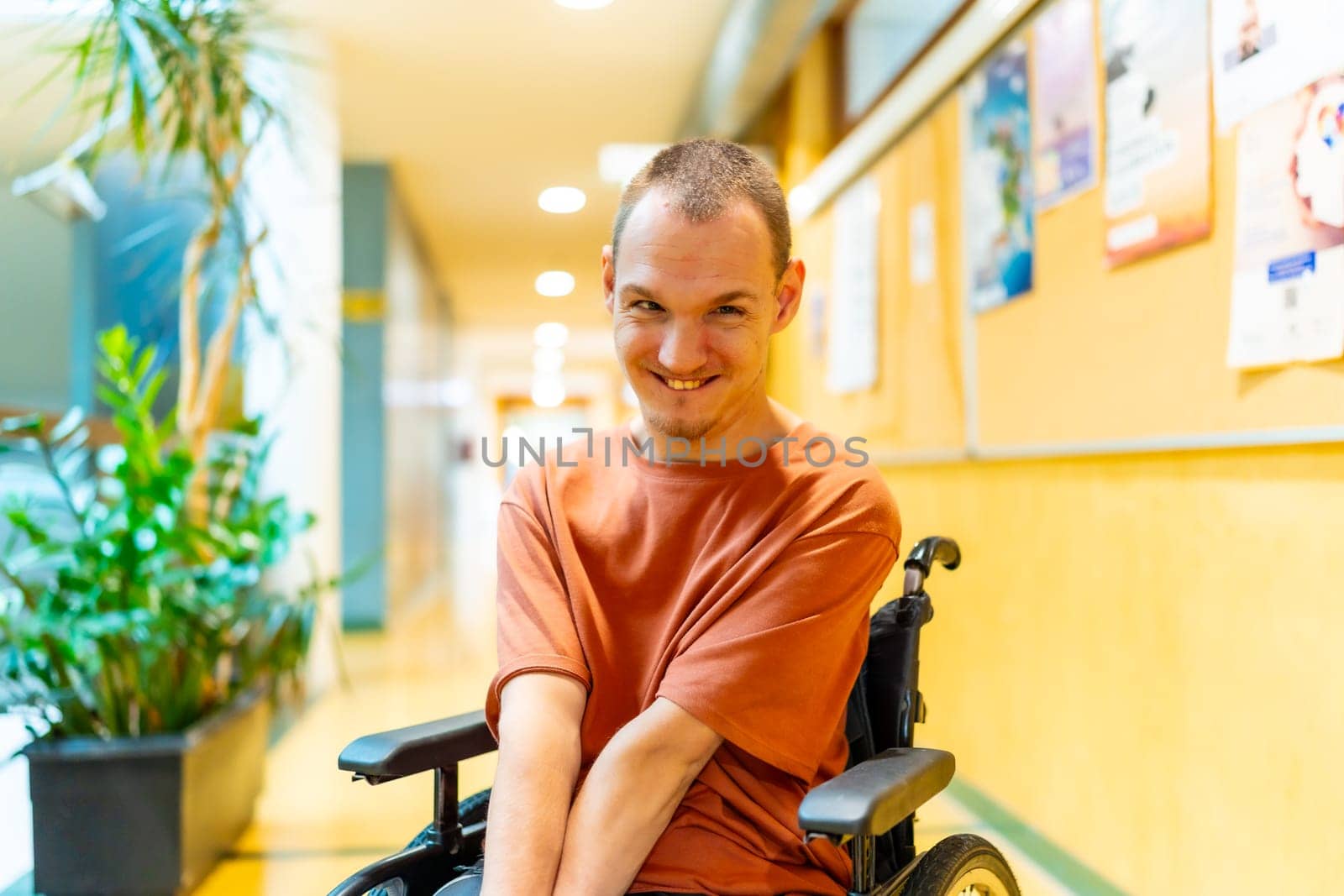 Man with disability sitting in wheelchair smiling at camera in the corridor of coworking
