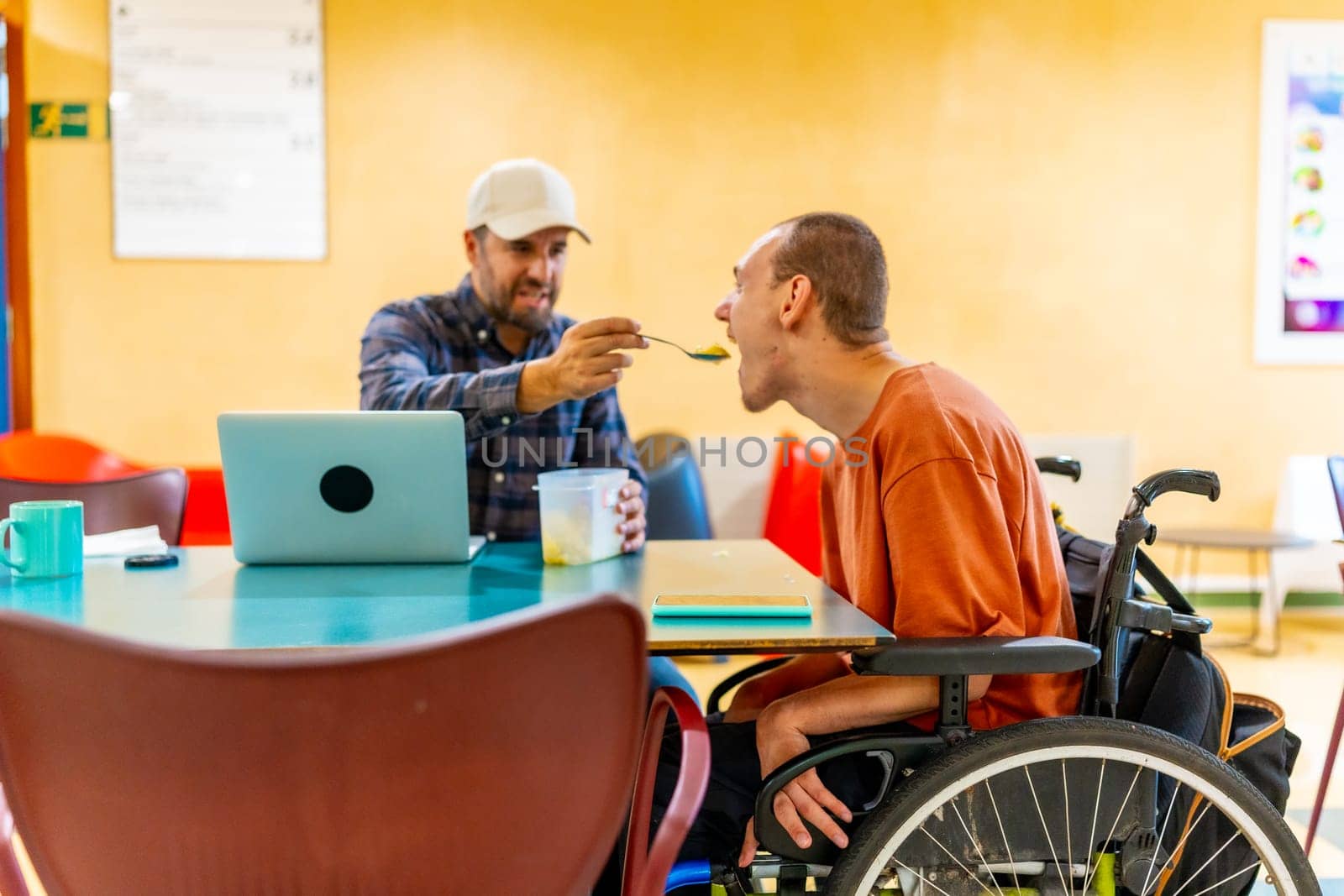 Colleague feeding a man with cerebral palsy in a coworking cafeteria in a modern space