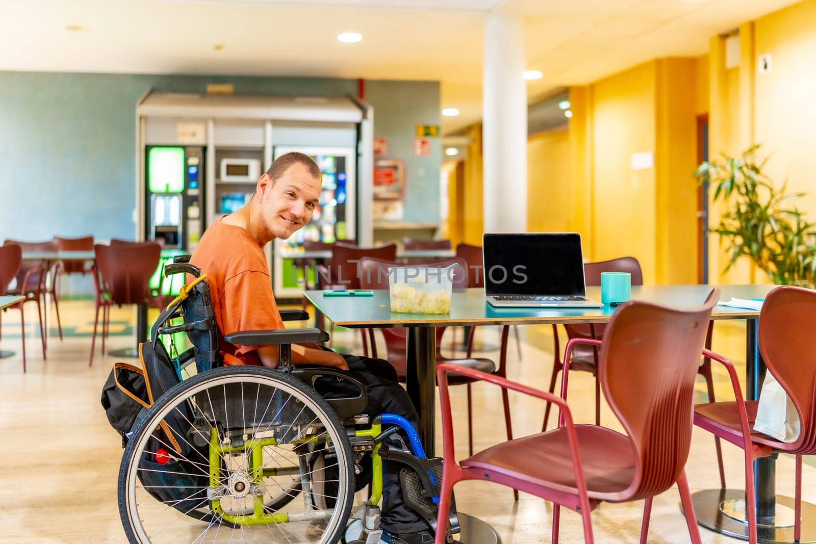 Horizontal full lenght photo of a caucasian adult man with disability in wheelchair in a dinning room in coworking
