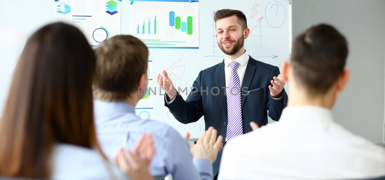 Young handsome teacher man in suit with workgroup seminar board with chart coaching background. Lecturer for applicants retraining financial statistics management enterprise etiquette corporate spirit