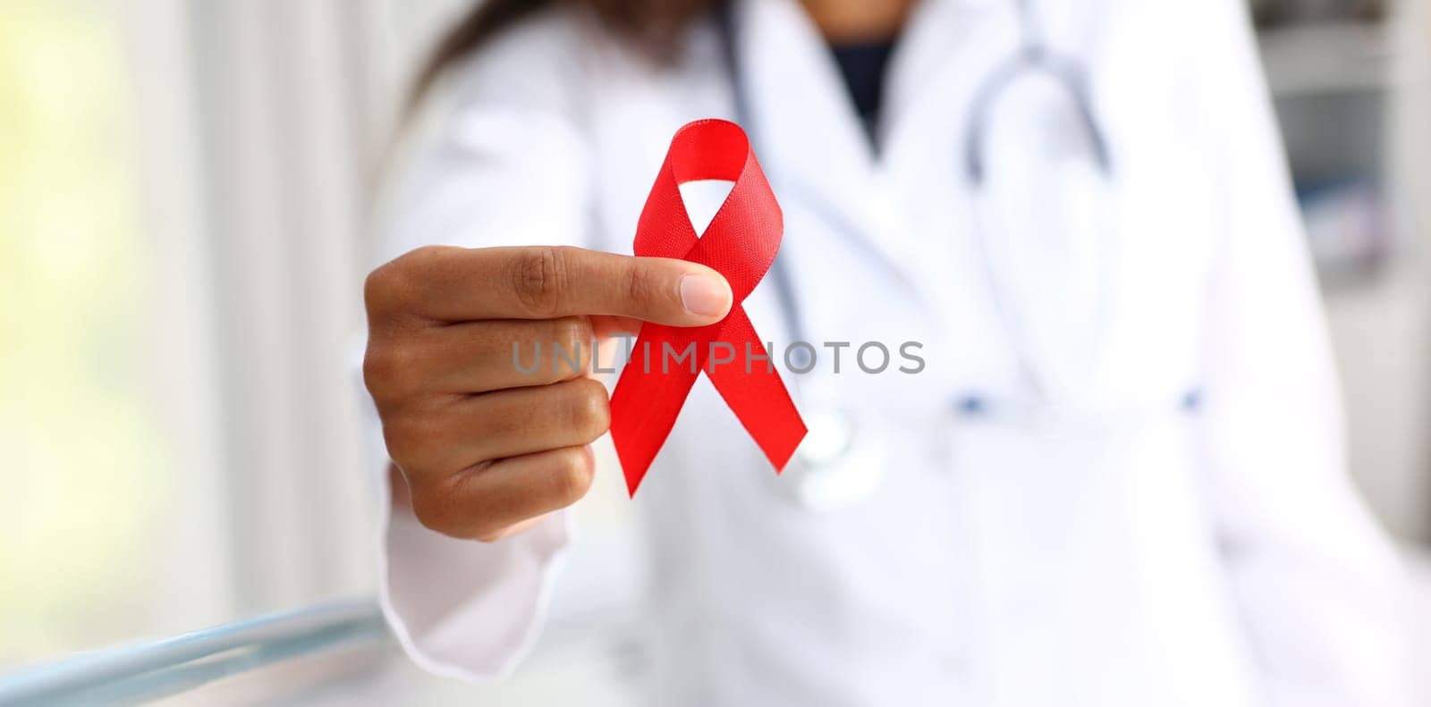 Black woman doctor holding a red ribbon in his hand an international day of protecting people from cancer by symbol of struggle and survival mankind