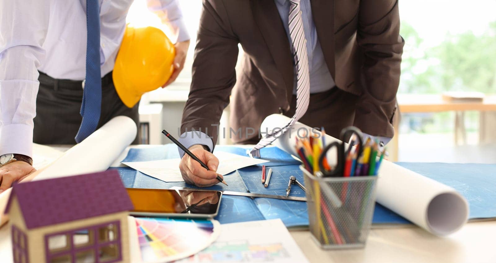 Architect Engineer Team Work on Building Draft. Two Professional Builder Holding Yellow Hardhat Designing House Model on Blueprint Using Pencil. Measuring Tools, Laptop at Workplace