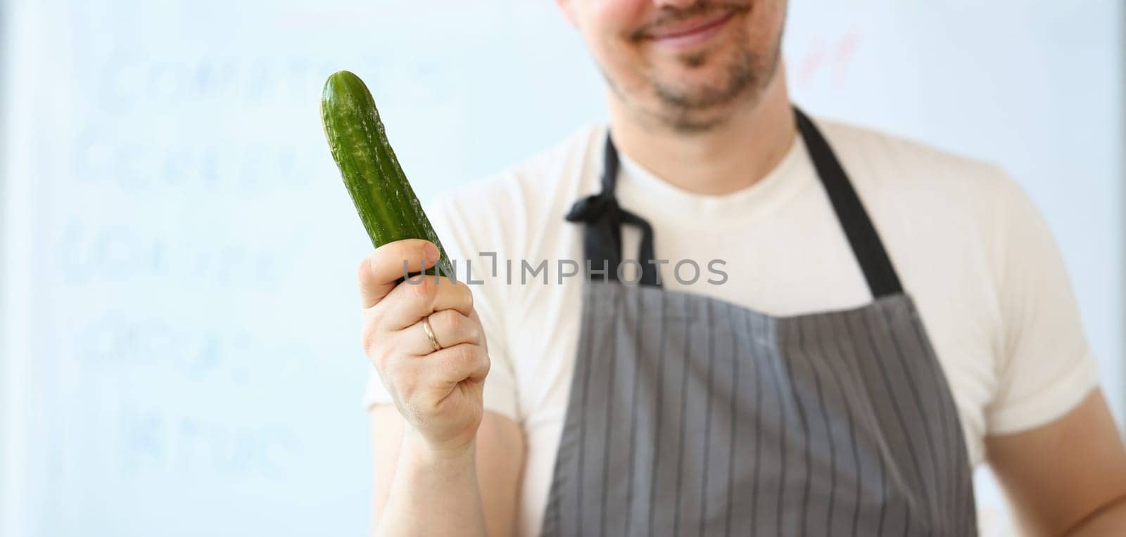 Smiling Chef Holding Raw Green Organic Cucumber. Beard Man Showing Fresh Vegetable on White Background. Male Hold Ingredient for Vegetarian Food. Healthy Vegan Lifestyle Horizontal Photography