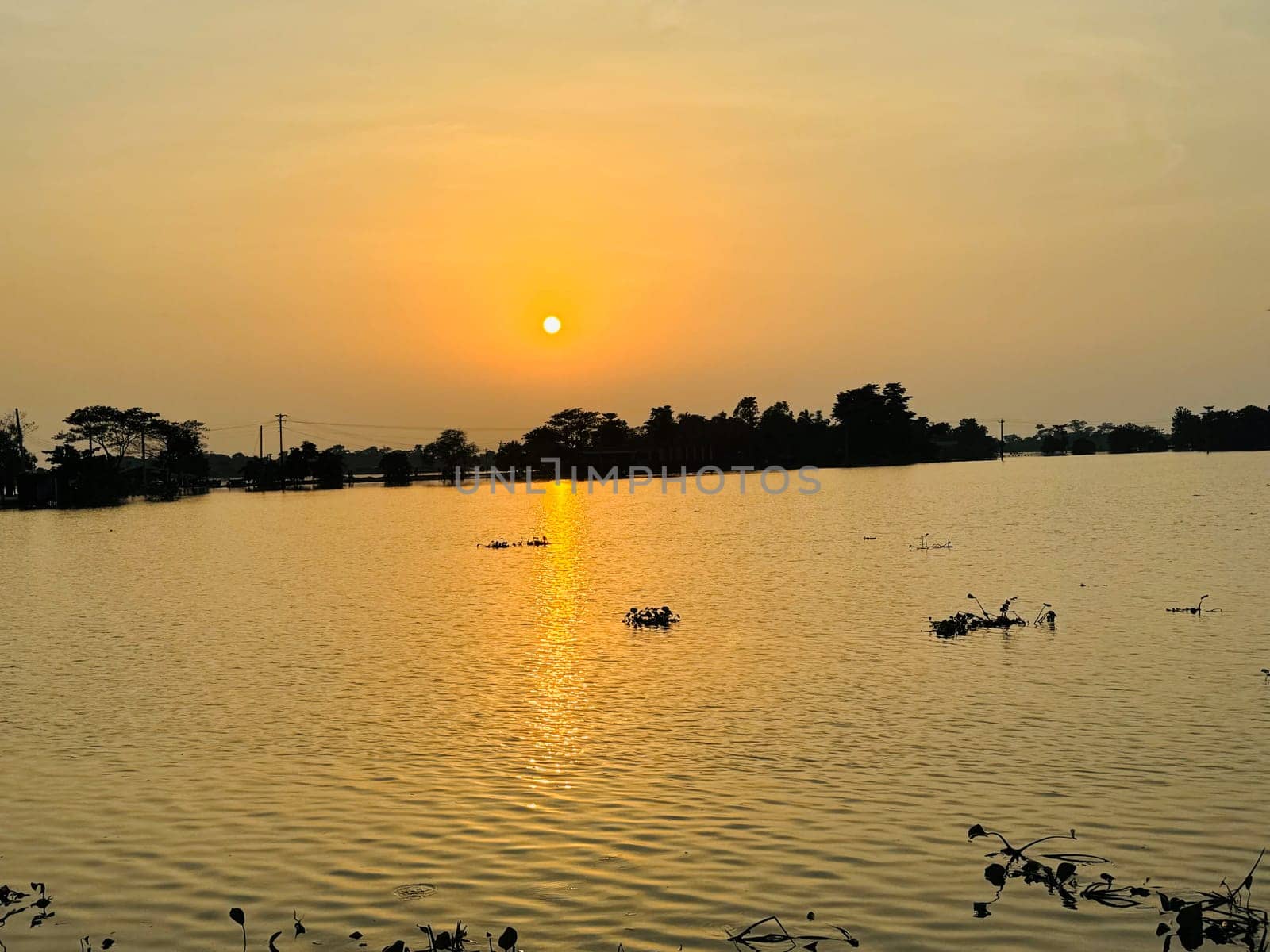 A breathtaking view of the sun setting over a tranquil lake, casting warm hues across the water and sky. This stunning scene is perfect for use in romantic, nature, and landscape projects.