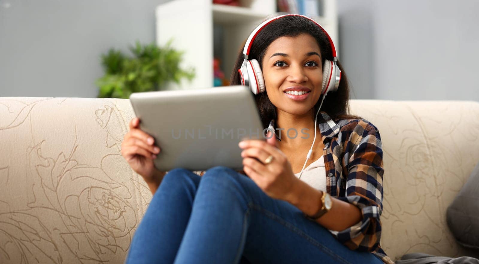 Black ordinary female american teen portrait at home sofa remote education concept. Girl hold tablet in hand music apps teacher checks homework online university library learning foreign languages