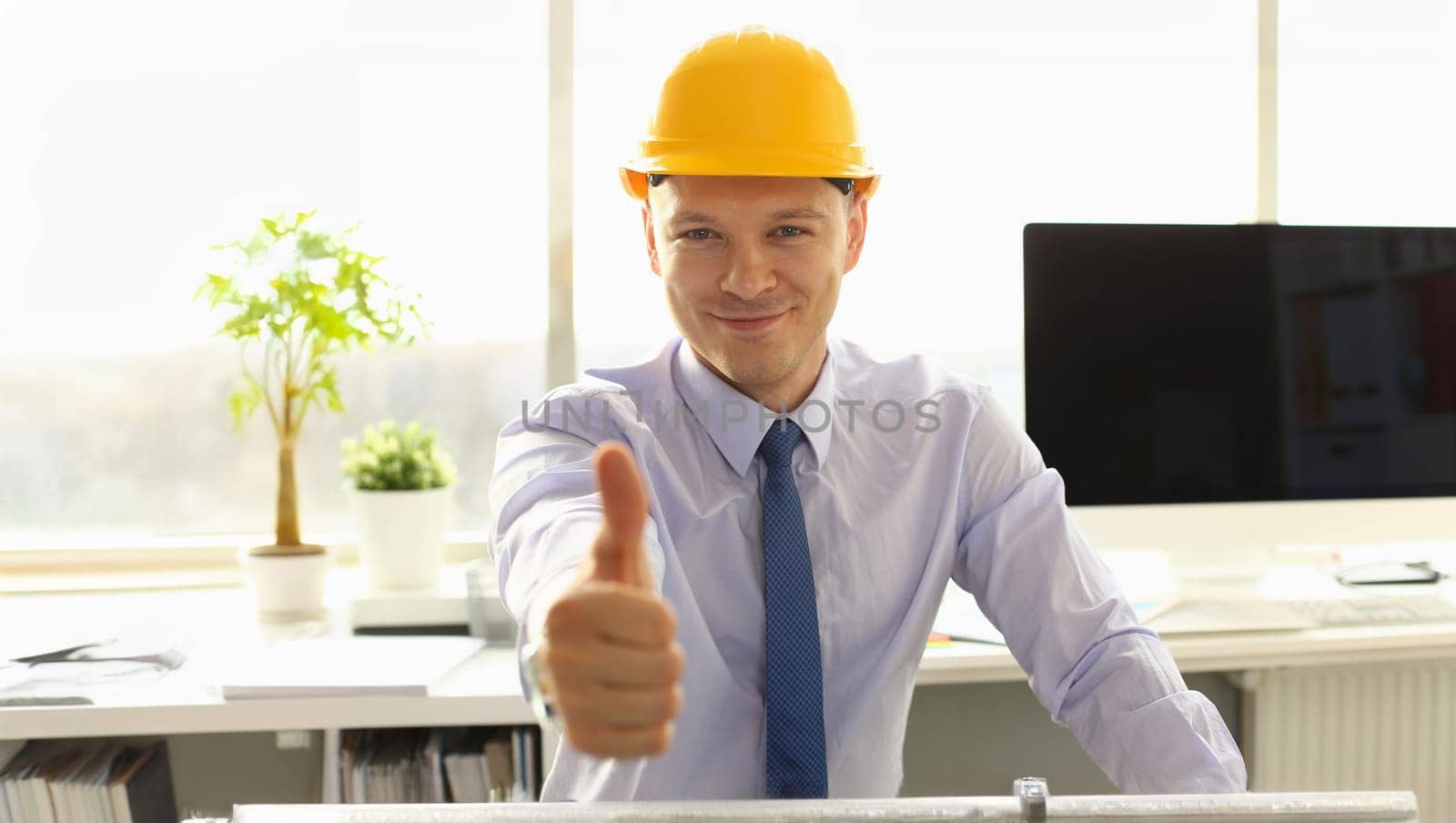 Handsome Arschitect Thumb Up in Engineering Office. Young Foreman in Yellow Hard Hat Sitting at Workplace Showing Agreed Sign. Project Engineer Specialist Wearing Formal Shirt and Tie