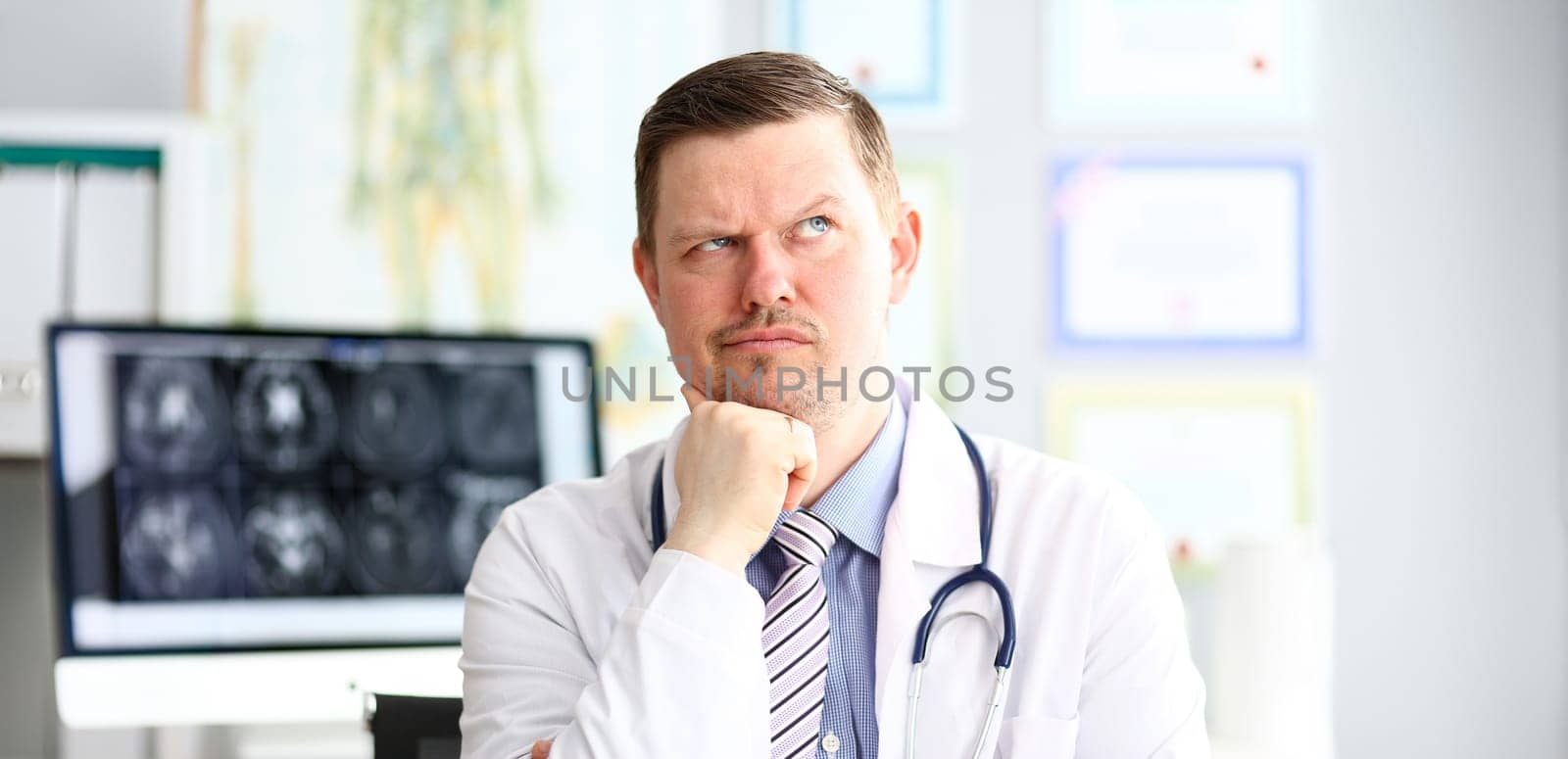 Male doctor with strange facial expression sit in his office headshot