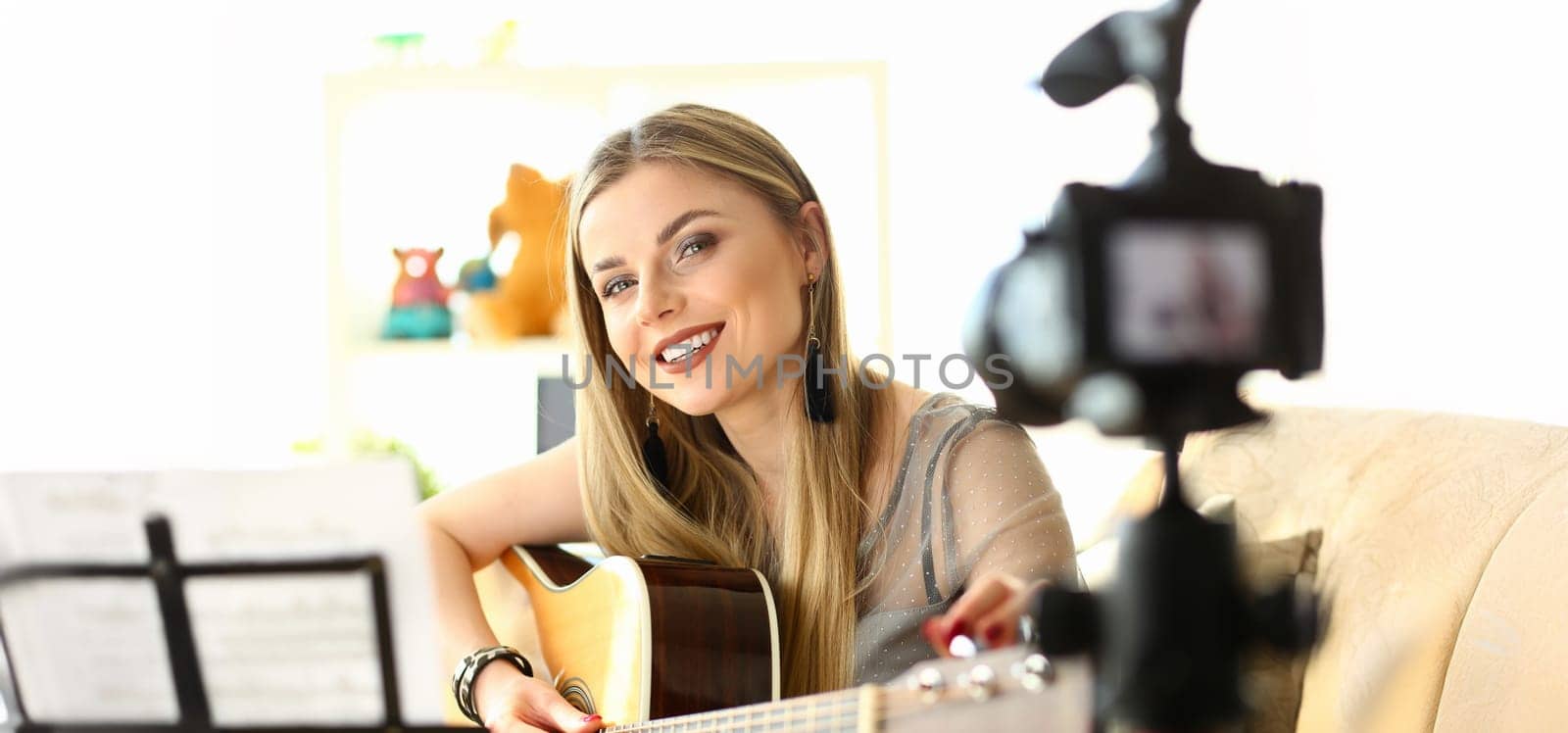 Trendy millenial beauty woman misic blogger hold in hand guitar sit on sofa couch. Online web broadcast internet on home background concept