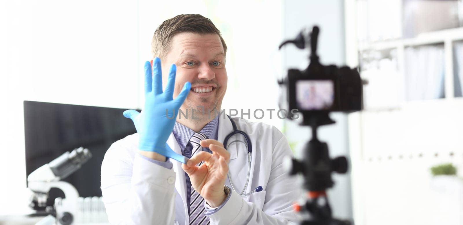 Funny smiling doctor demonstrative pulling on protective gloves on arm ready to give some medical advices to his subscribers portrait concept