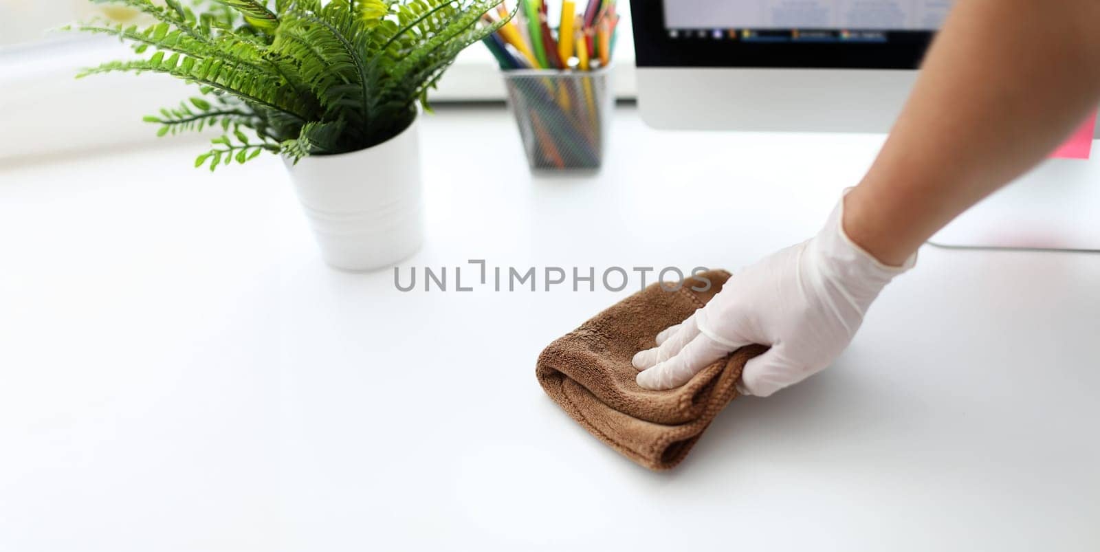 Focus on gloved male hand holding cloth and swiping all dirt and dust inhabited by harmful bacteria from white office table with concentration and diligence. Pleasant clean-up concept