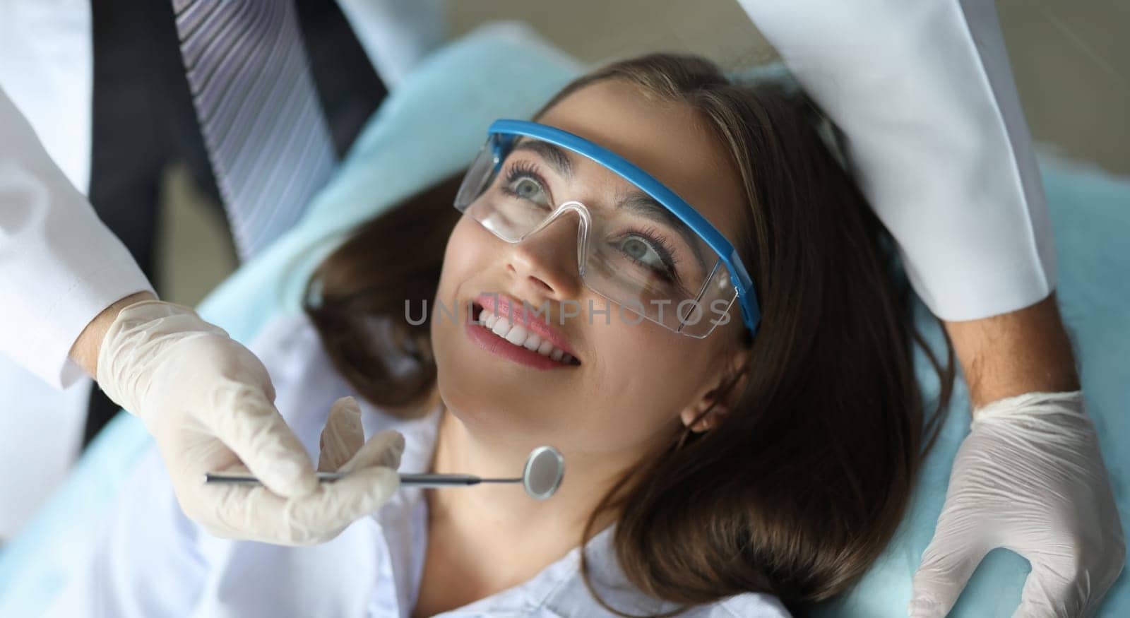 Close-up of smiling beautiful patient visiting annual doctor appointment. Wonderful female on examination with mirror of stomatologist. Healthcare and dentist concept