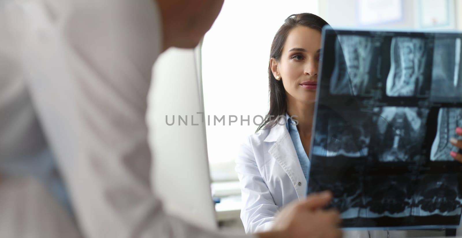 Portrait of serious surgeon looking carefully on spine x-ray in different projections. Cute doc discussing disease diagnosis with colleague. Healthcare concept
