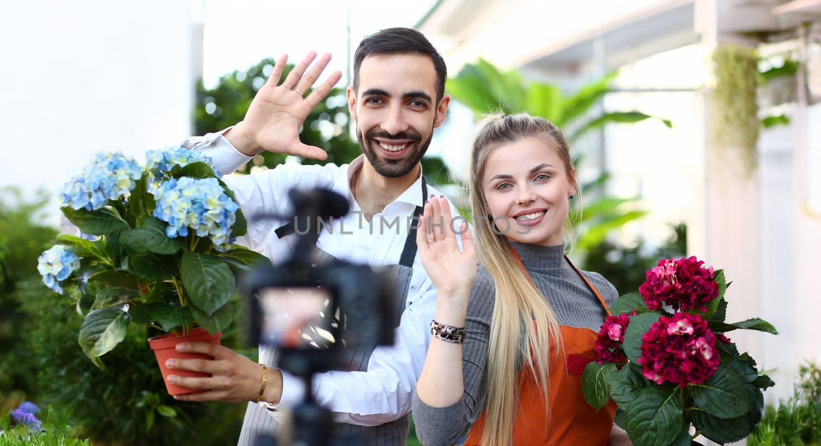 Young millennial family say hallo subscribe to the channel put likes and wave to their subscribers on the channel aganist greenhouse background. Social media marketing luck concept.
