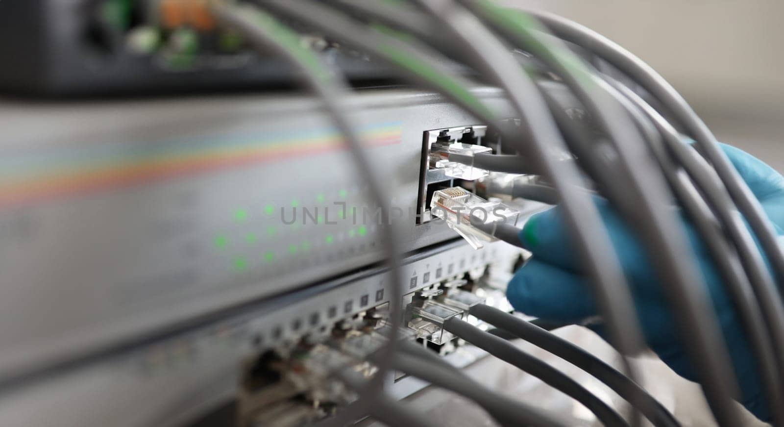 Service and networking database concept .Male technician hand in blue protective glove connects set cable connector to switch closeup.