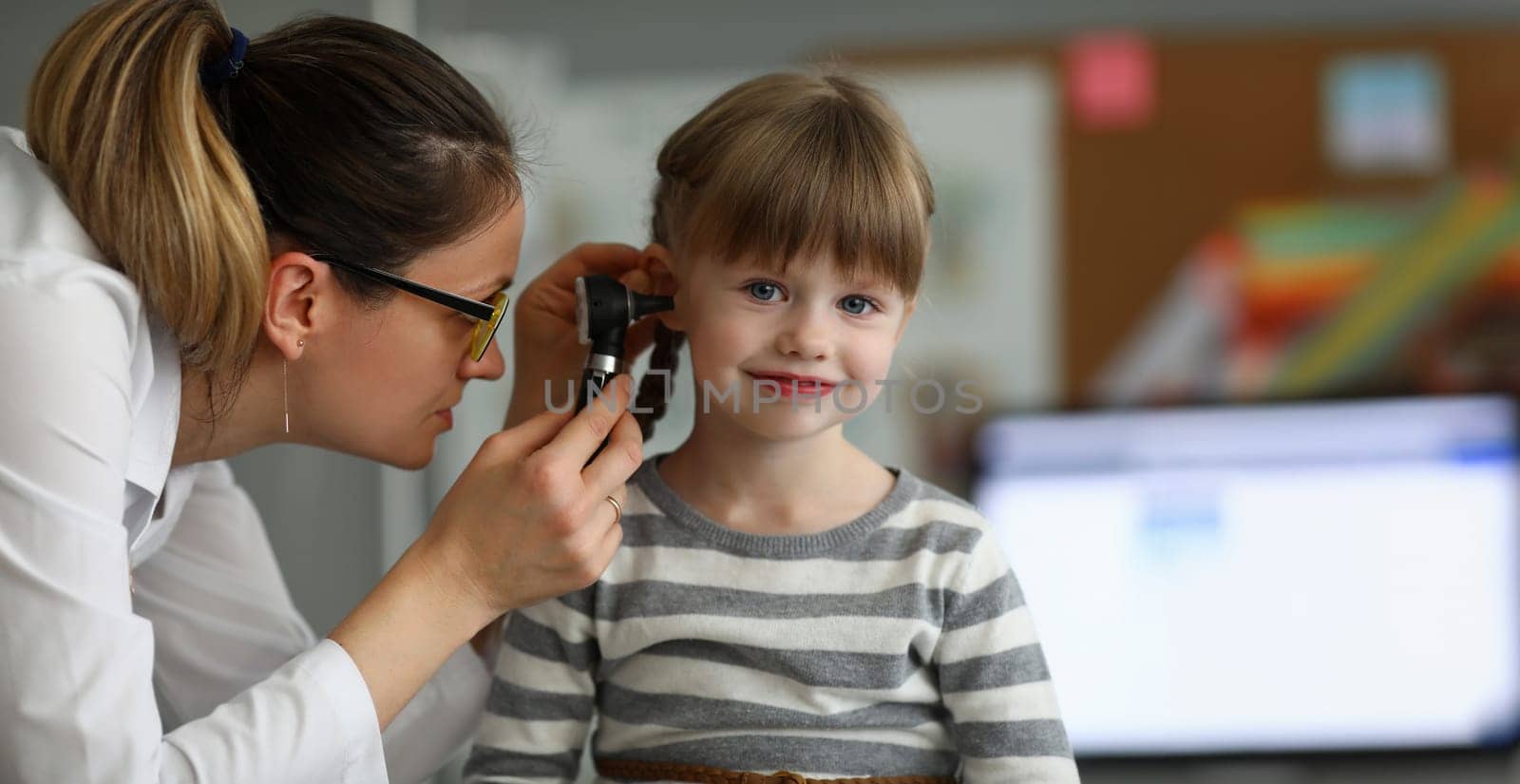 Pediatrician examines ear of sick child in office of hospital background. Otitis Prevention Concept