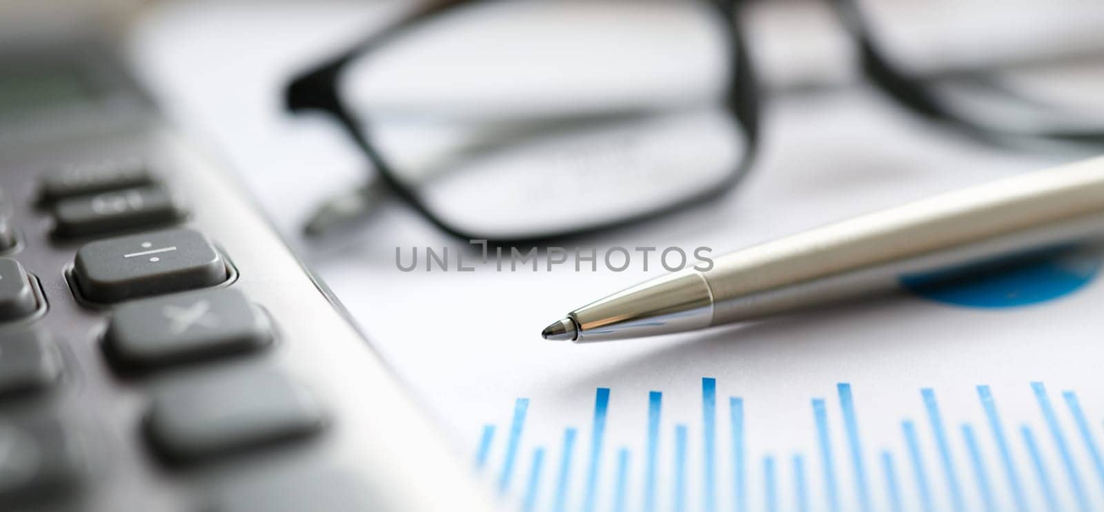 Silver pen gray calculator with paper chart and glasses lie in office table closeup. Business education concept