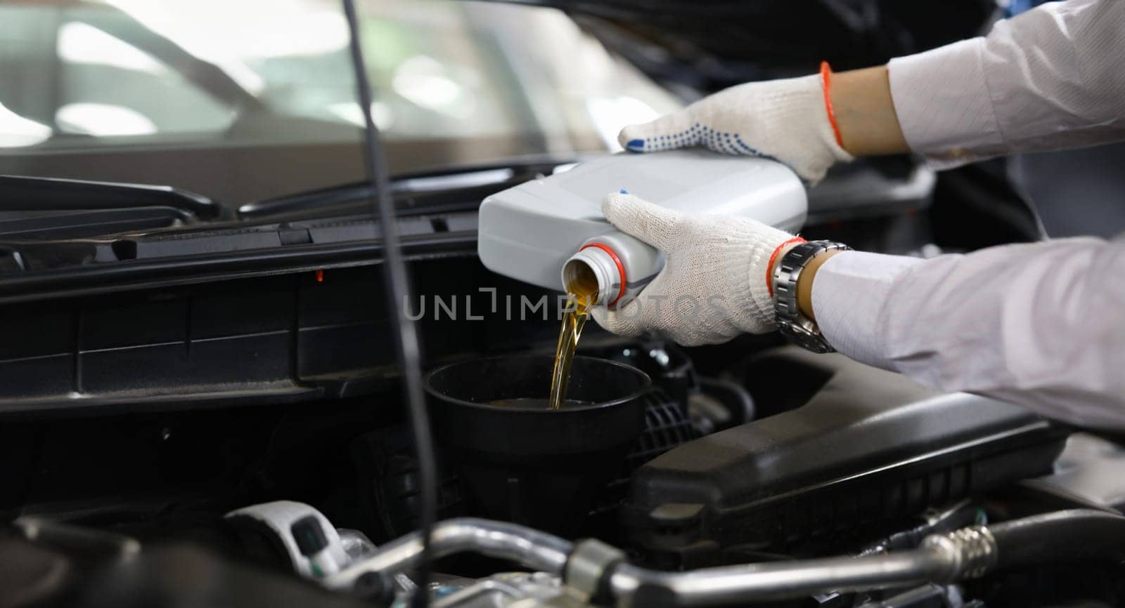 Focus on auto mechanic in gloves replacing and pouring fresh oil into engine at automobile service station. Vehicle inspection concept. Blurred background