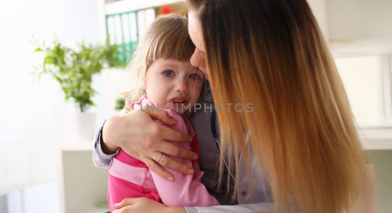 Doctor hugging scared crying little baby girl visiting her office portrait