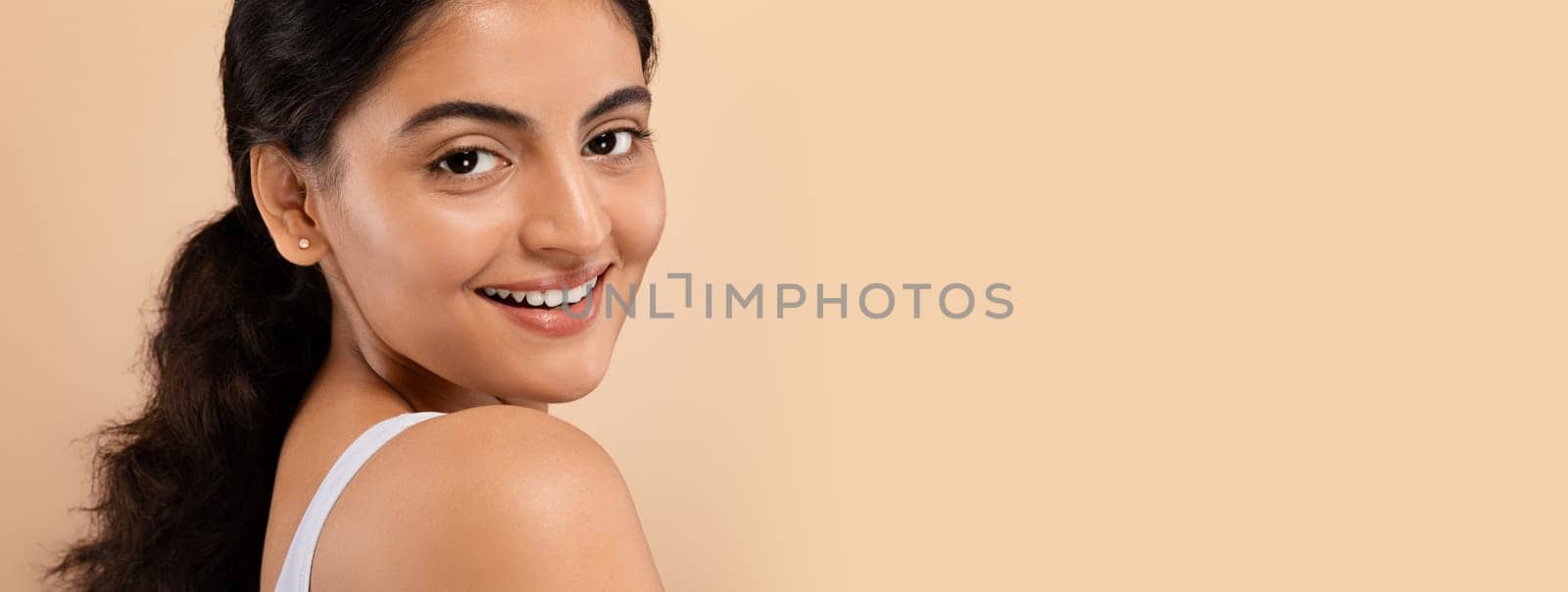 Closeup Shot Of Attractive Young Indian Woman With Beautiful Skin, Portrait Of Smiling Eastern Lady With Natural Beauty Looking At Camera, Posing Isolated Over Beige Studio Background, Free Space