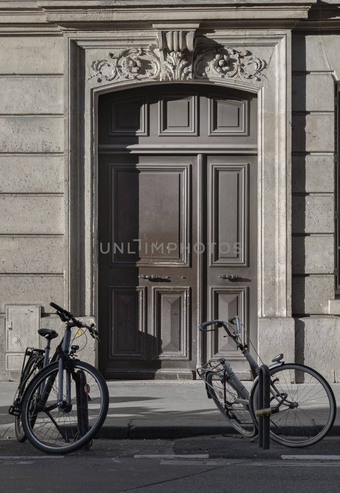 France, Paris - Jan 05, 2024 - Two bicycle parked at the side of the edge of road in front Traditional french building in downtown Paris. Brown wooden door entrance of old building with two Bicycle parked in front, Classical architecture of Antique building, Space for text, Selective focus.