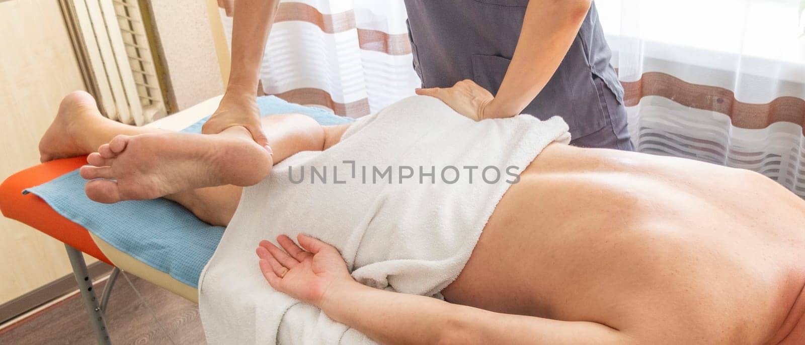 Female manual therapist performing physical therapy on mid aged male patient.