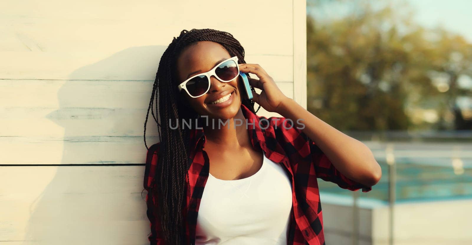 Happy cheerful African american young woman smiles calling on phone, black girl talking on the smartphone looking away in the city