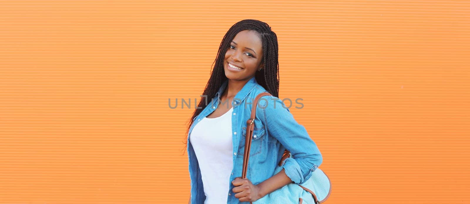 Portrait of happy stylish young african woman in casual clothing, glasses with dreadlocks, backpack posing in the city