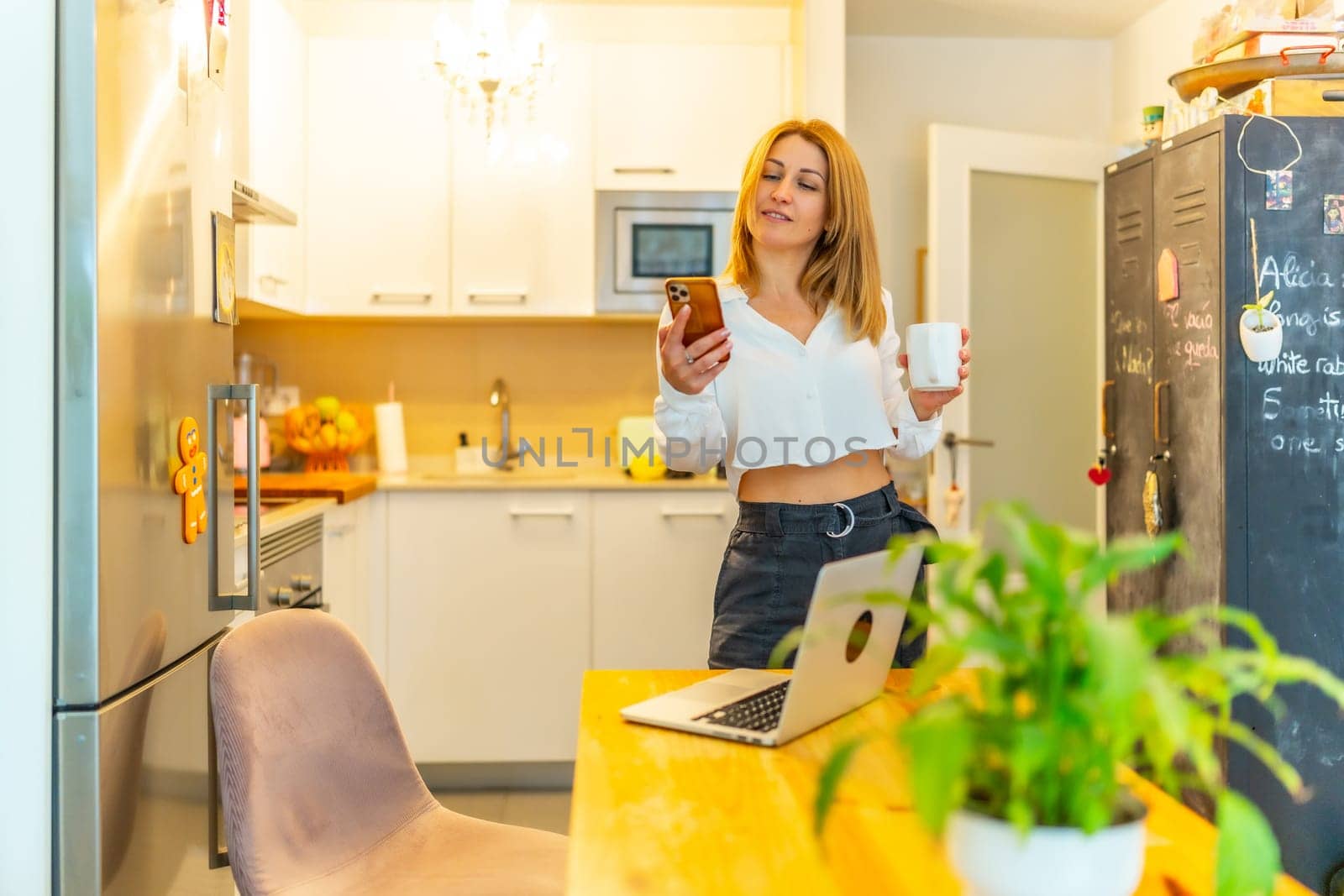 Blonde casual adult businesswoman using phone during coffee break working from home