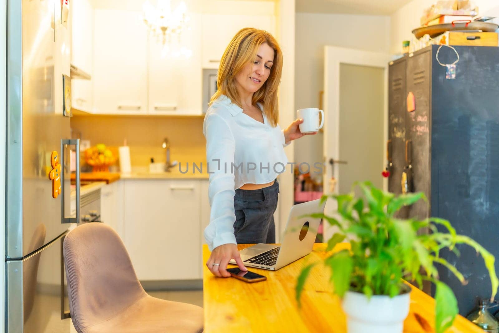 Blonde caucasian adult businesswoman checking the mobile phone during coffee break working at home