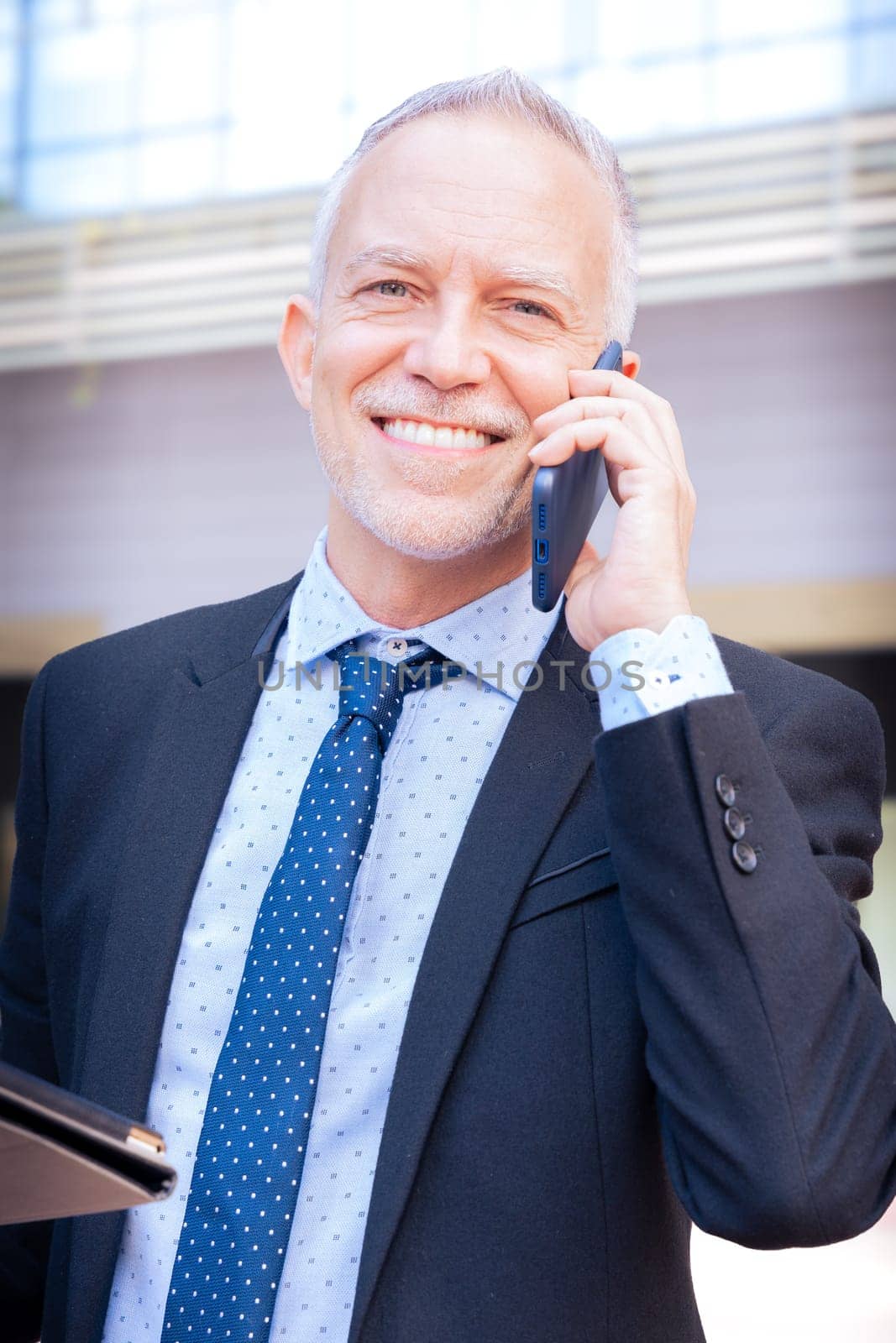 Satisfied with the results, the businessman walks down the street outside the office building, a mature boss holds a phone looking at camera.
