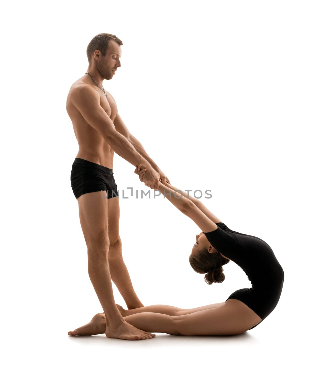 Athletic young male acrobat making exercises in pair with a young girl in studio isolated shot