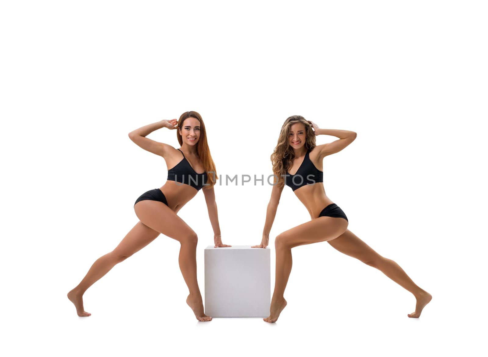 Pretty girls in black tops and shorts posing together by the cube studio shot