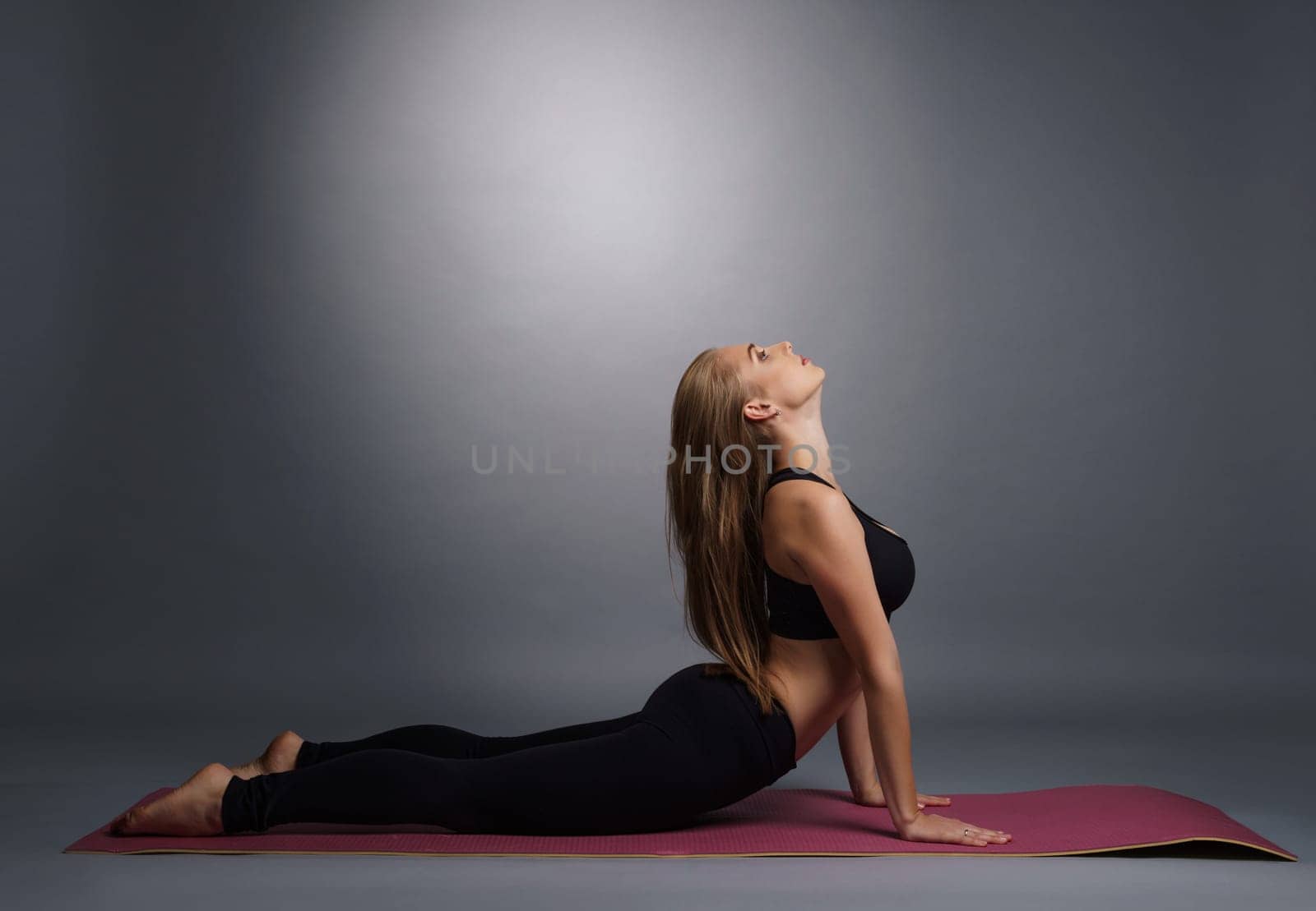 Pretty young fitness trainer in black top and leggings exercising on mat in studio