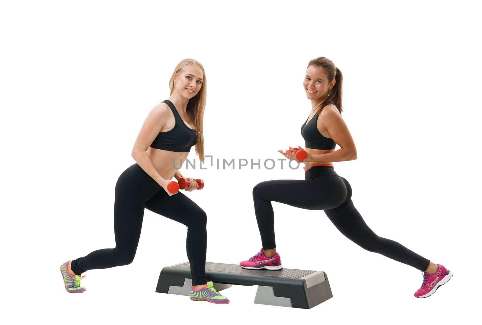 Step-aerobics, fitness and shaping concept - two young energetic sporty women in sportswear exercising with dumbbells and stepper on white isolated background