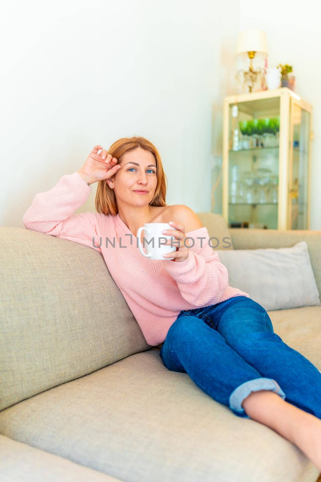 Vertical portrait of a mature woman sitting on the sofa with coffee cup