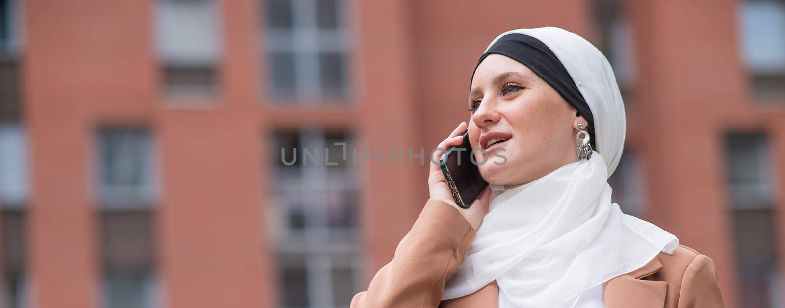 Young woman in hijab talking on smartphone outdoors. Widescreen