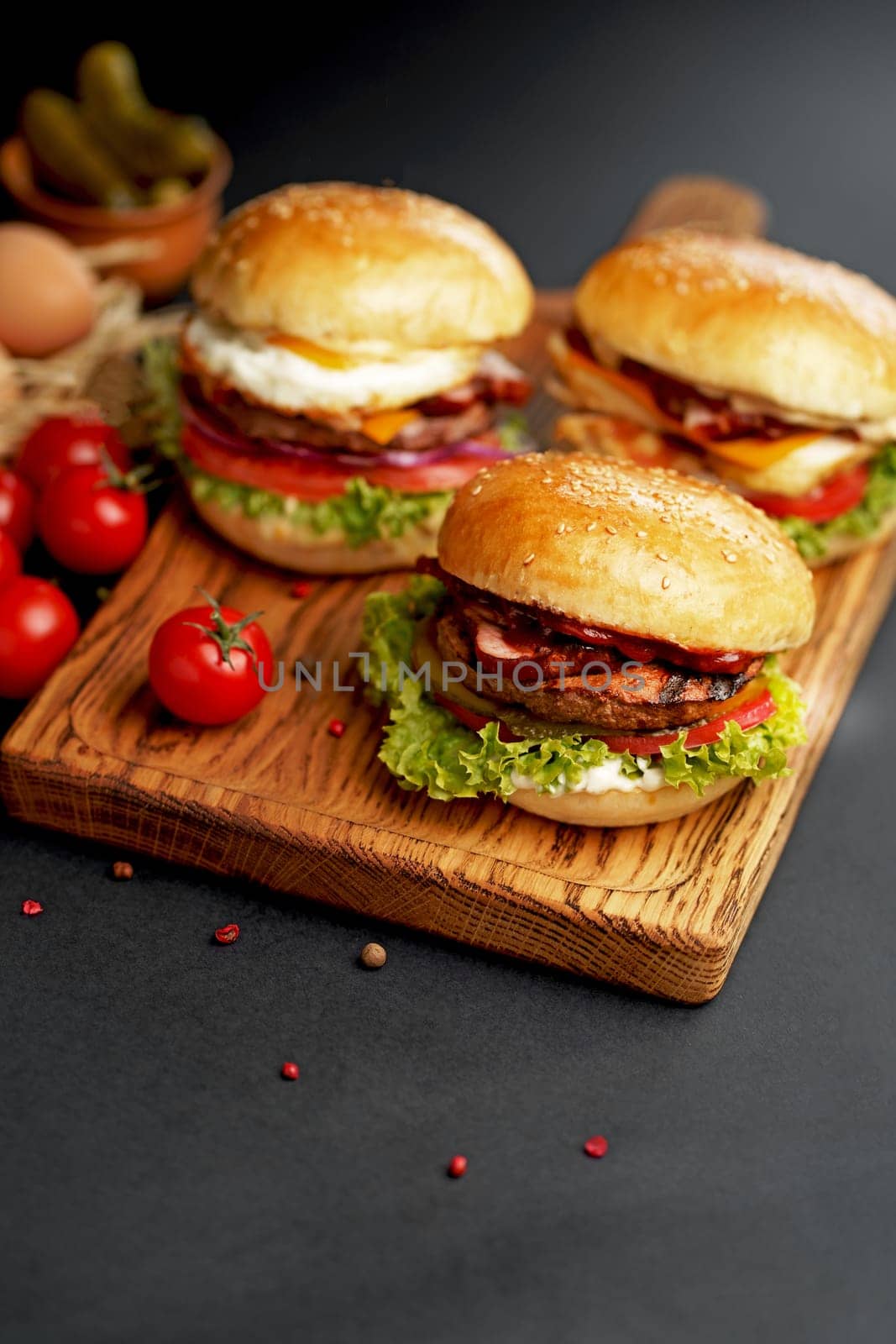 Close-up of a delicious fresh homemade burger with lettuce, cheese, onion and tomato on a rustic wooden board on a dark background by aprilphoto