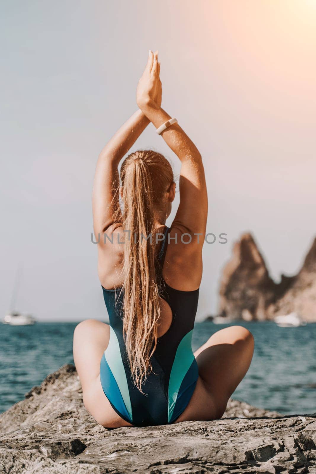 Yoga on the beach. A happy woman meditating in a yoga pose on the beach, surrounded by the ocean and rock mountains, promoting a healthy lifestyle outdoors in nature, and inspiring fitness concept. by Matiunina