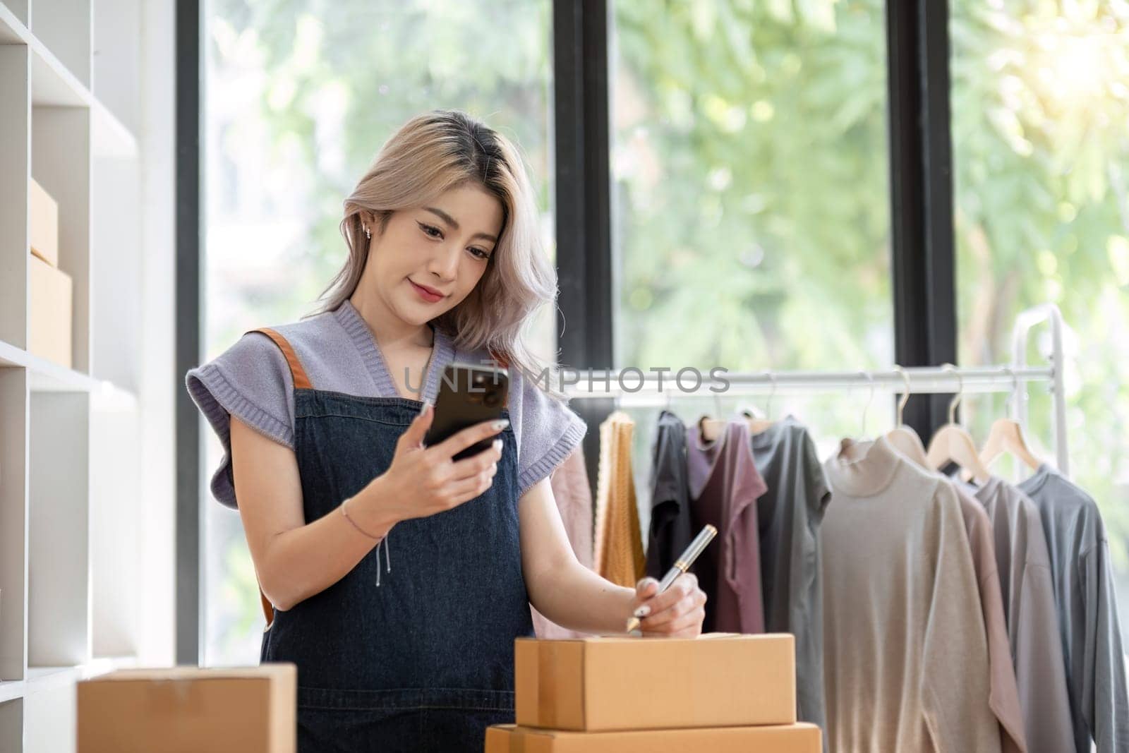 Female entrepreneur writing on the parcel after talking on the phone standing and writing on the parcel on the table online seller concept.