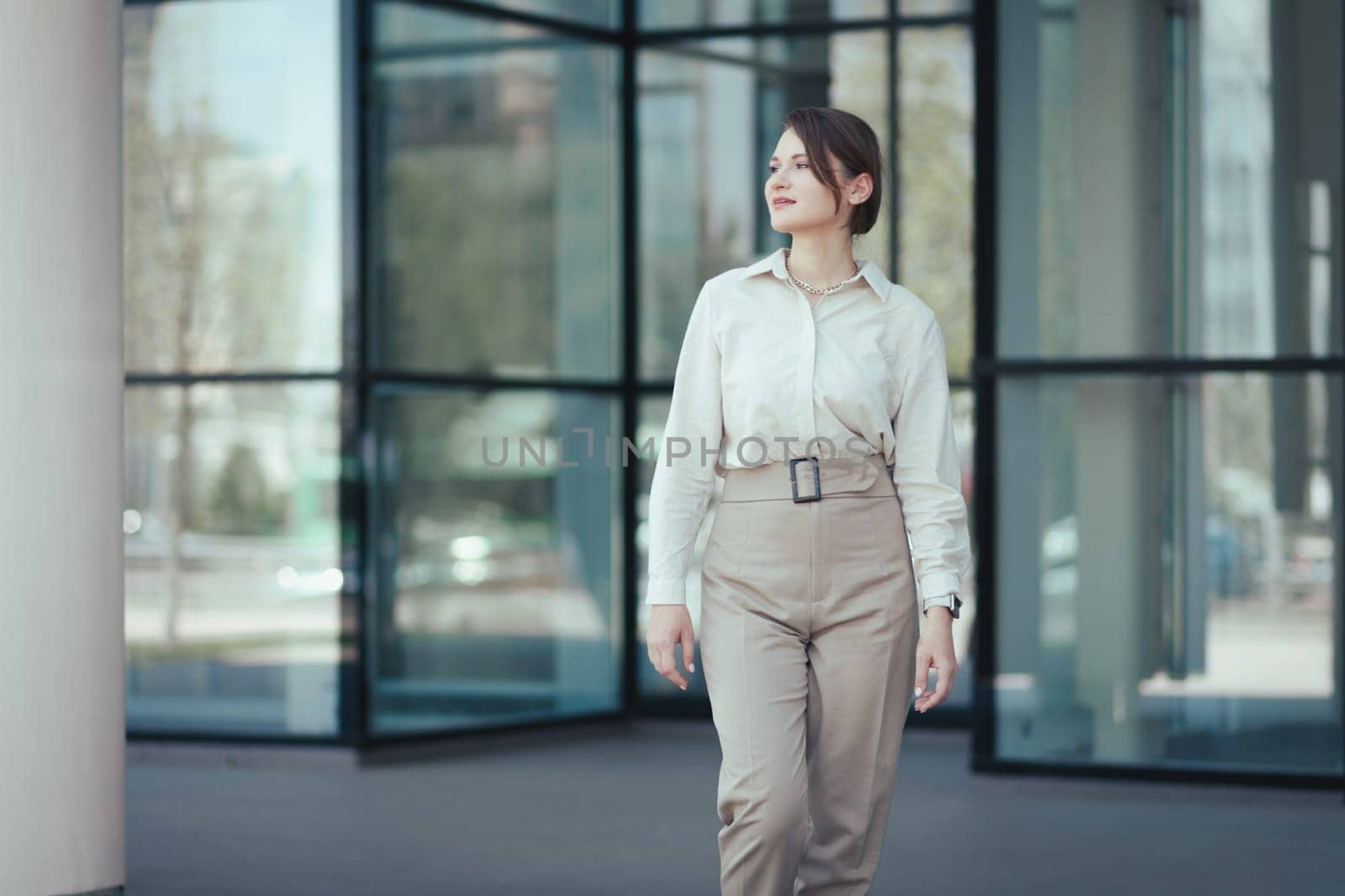 Portrait of a successful business woman in a business suit comes out of a modern business building, looks to the side.
