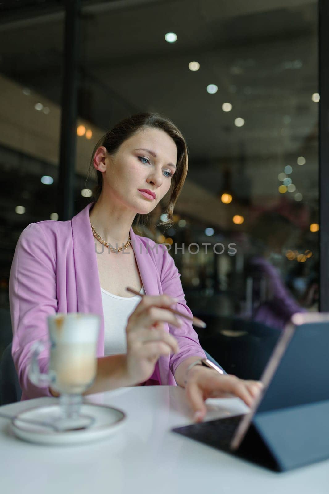 Stylus from a tablet in a woman's hand in front of a tablet on a table in cafe, copy space, vertical.