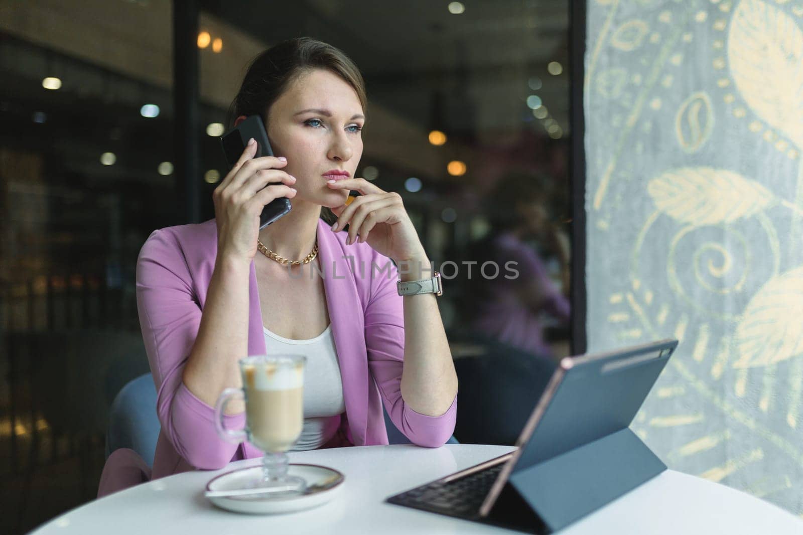 A young businesswoman seriously and thoughtfully speaks on the phone in a cafe, discusses important matters of the company.