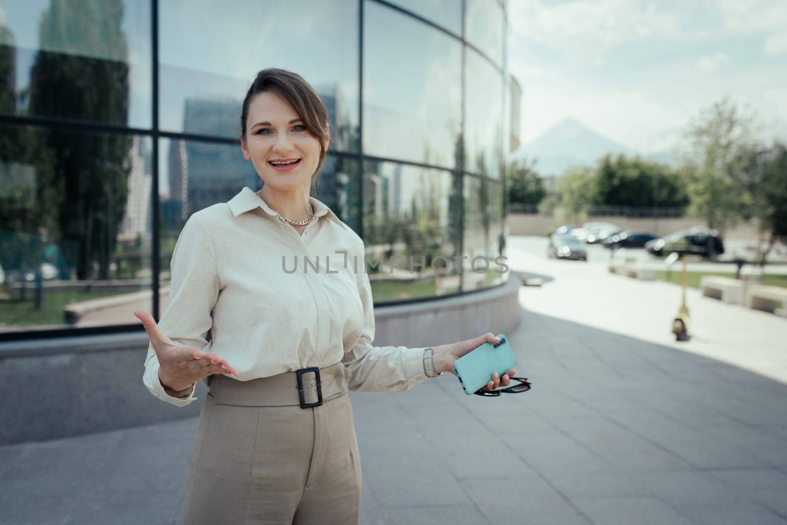 Joyful woman with outstretched hands outdoor portrait in business office style with phone in hand in the city street.