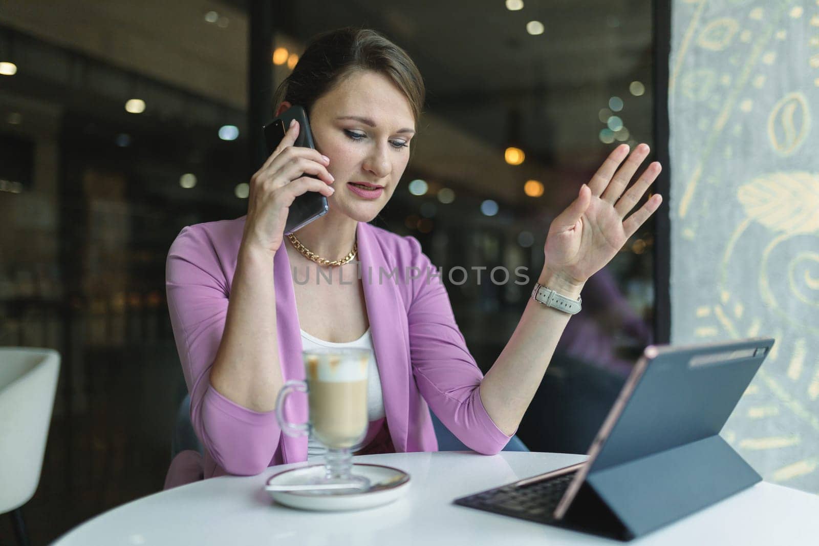 Young business woman solves business issues remotely by phone while sitting in a cafe by Rom4ek