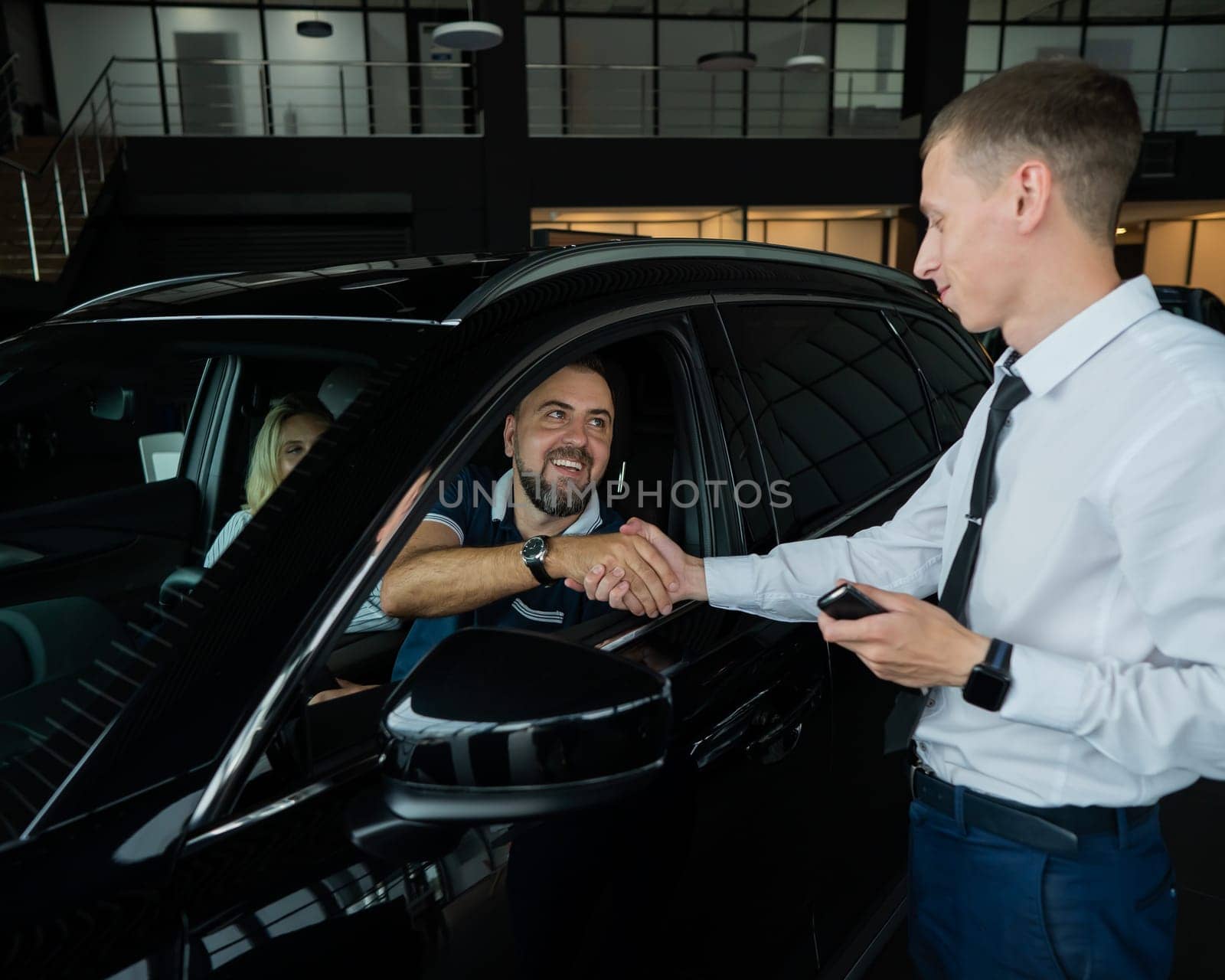 A caucasian couple shakes hands with a salesperson while buying a car. by mrwed54