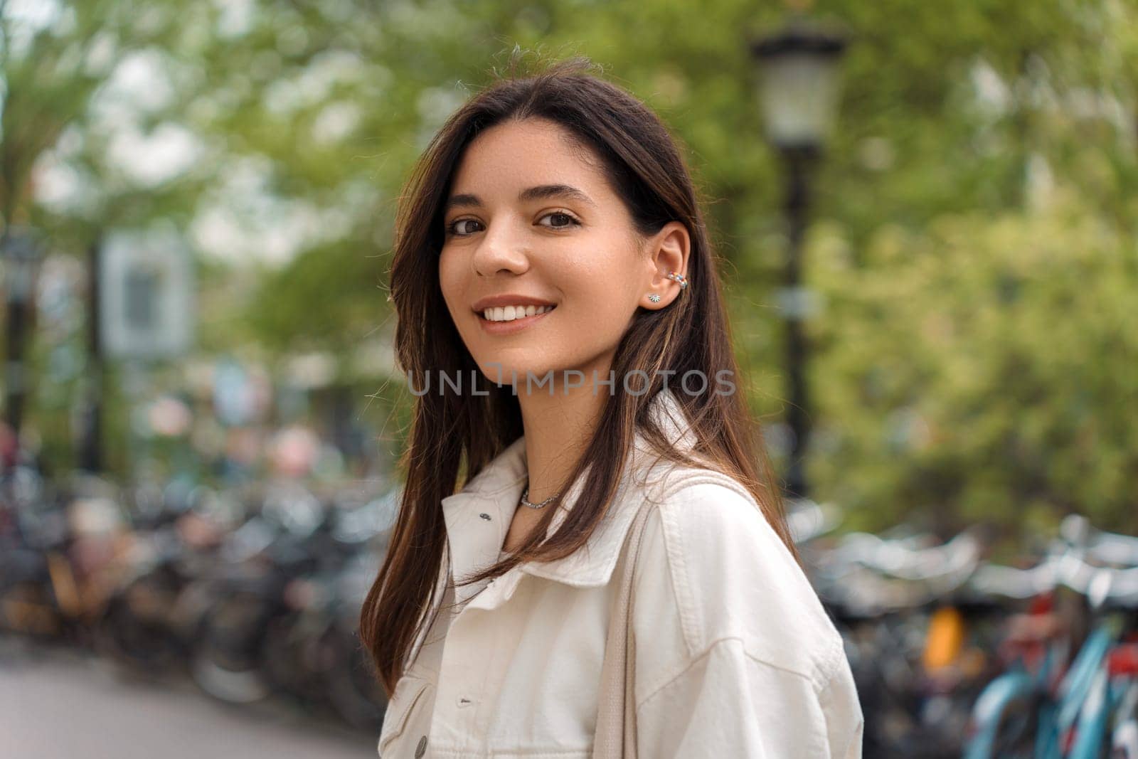 Radiating confidence, a young woman poses against the iconic backdrop of Amsterdam's charming streets, with bicycles weaving the essence of city life.